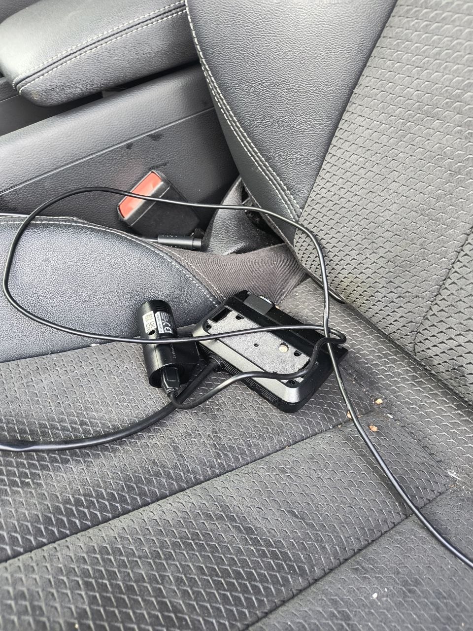 Dashcam mounting bracket, fuse tap, and connectors lying on the rear seat of the salvaged car after being removed from the windscreen and dashboard.