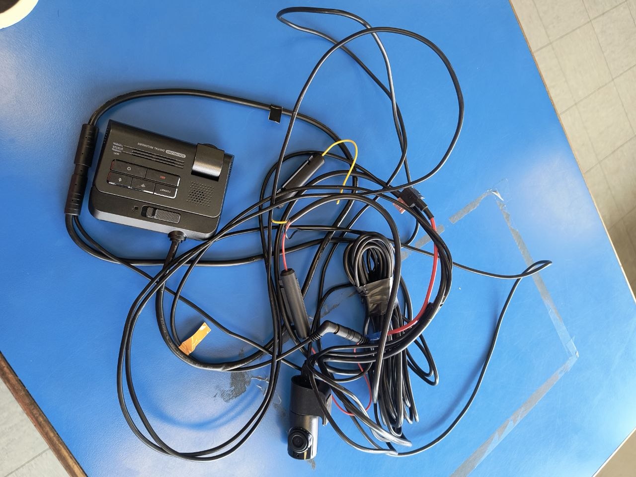 Dashcam head unit, front and rear cameras, and the complete wiring loom laid out on a blue table at Copart Sandwich after recovery from a written-off car.